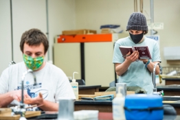 two students in the lab with masks, on of the reading a book